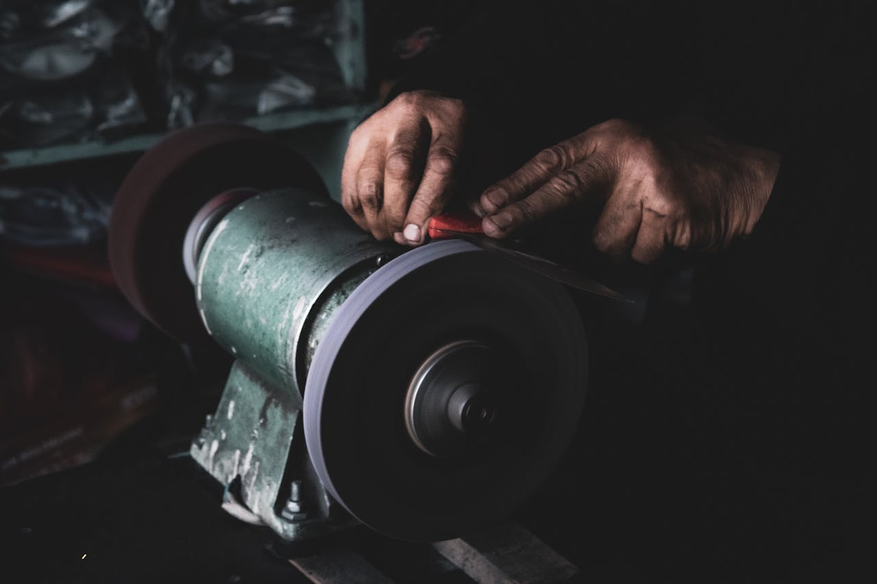 our-experience Detailed shot of hands carefully sharpening a blade using an electric grinder in a dimly lit workshop.