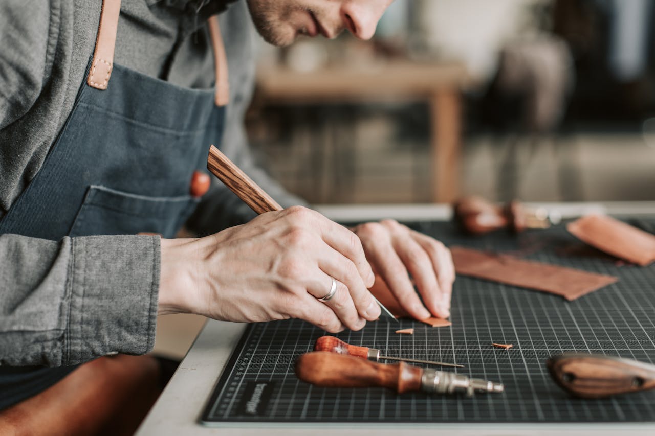 services-03 Close-up of an artisan skillfully crafting leather goods by hand in a workshop environment.