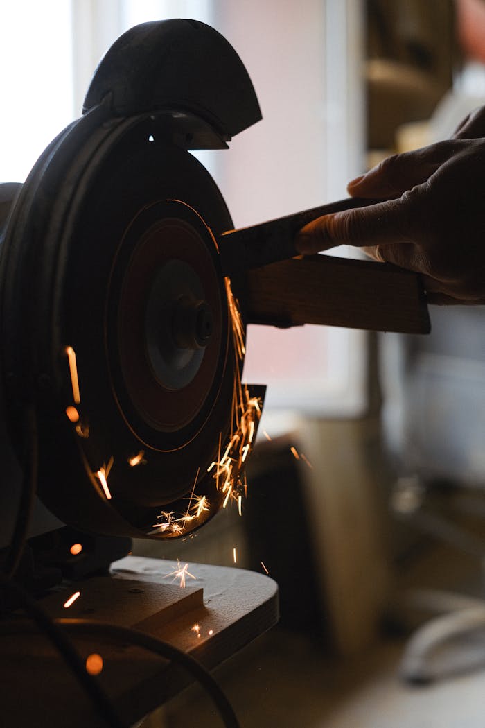contact-img Unrecognizable craftsman using grinding machine to sharpen detail while standing in workshop with sparks on blurred background during work process